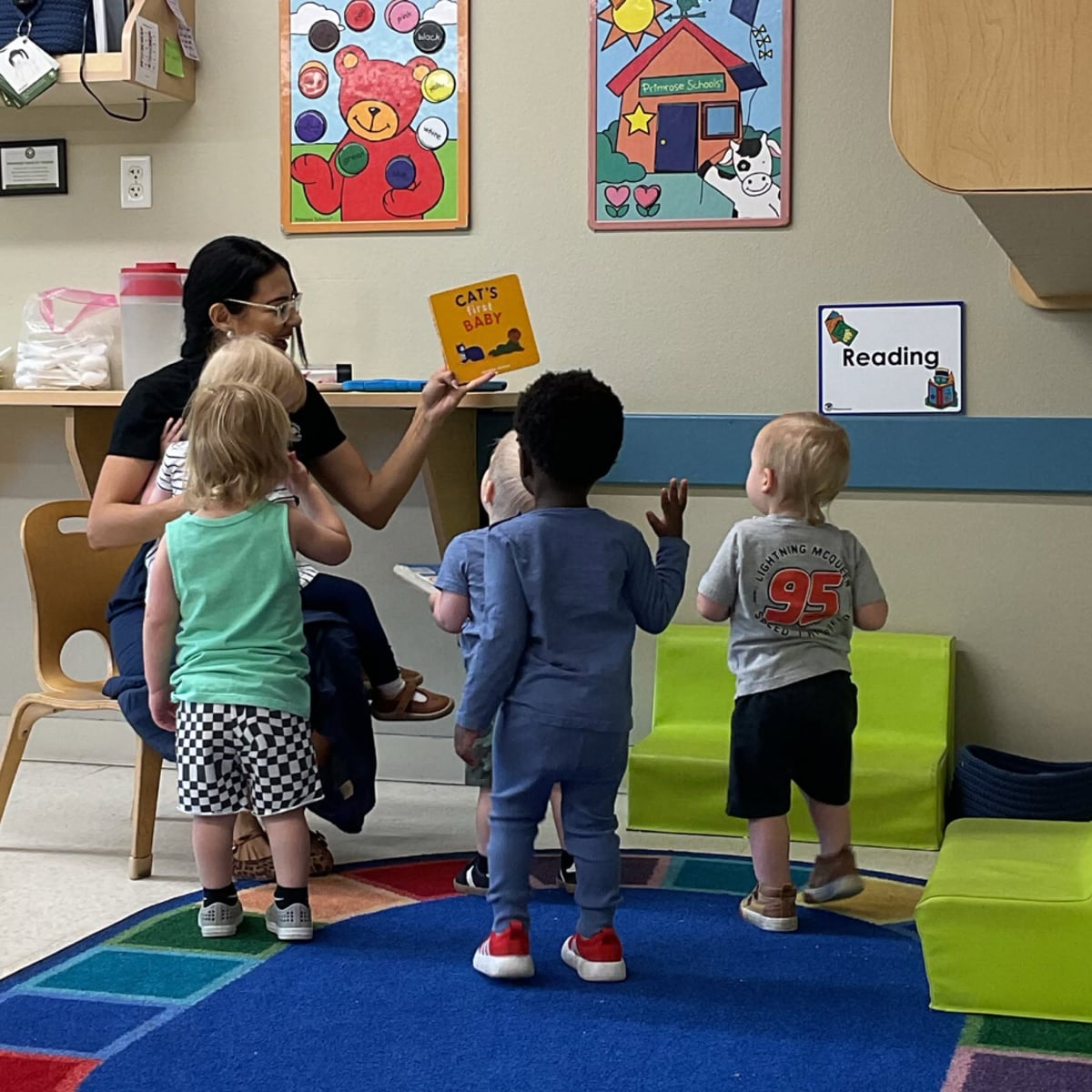 Teacher reading an interactive storybook to toddlers during group story time, encouraging listening skills, vocabulary development, participation, and a love of reading at Primrose School.