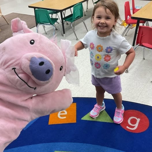 Toddler smiling while interacting with the Primrose Friend Percy® puppet, encouraging language development, confidence, imagination, and social-emotional learning at Primrose School.
