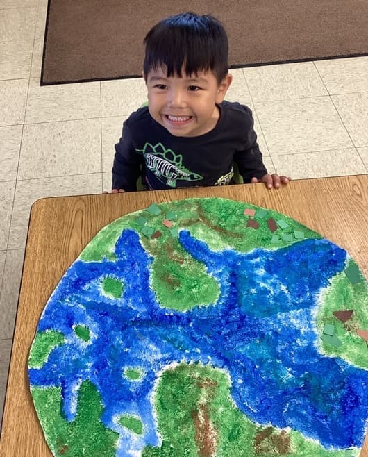 Child proudly displaying a handmade Earth craft while learning about geography, nature, and environmental stewardship.