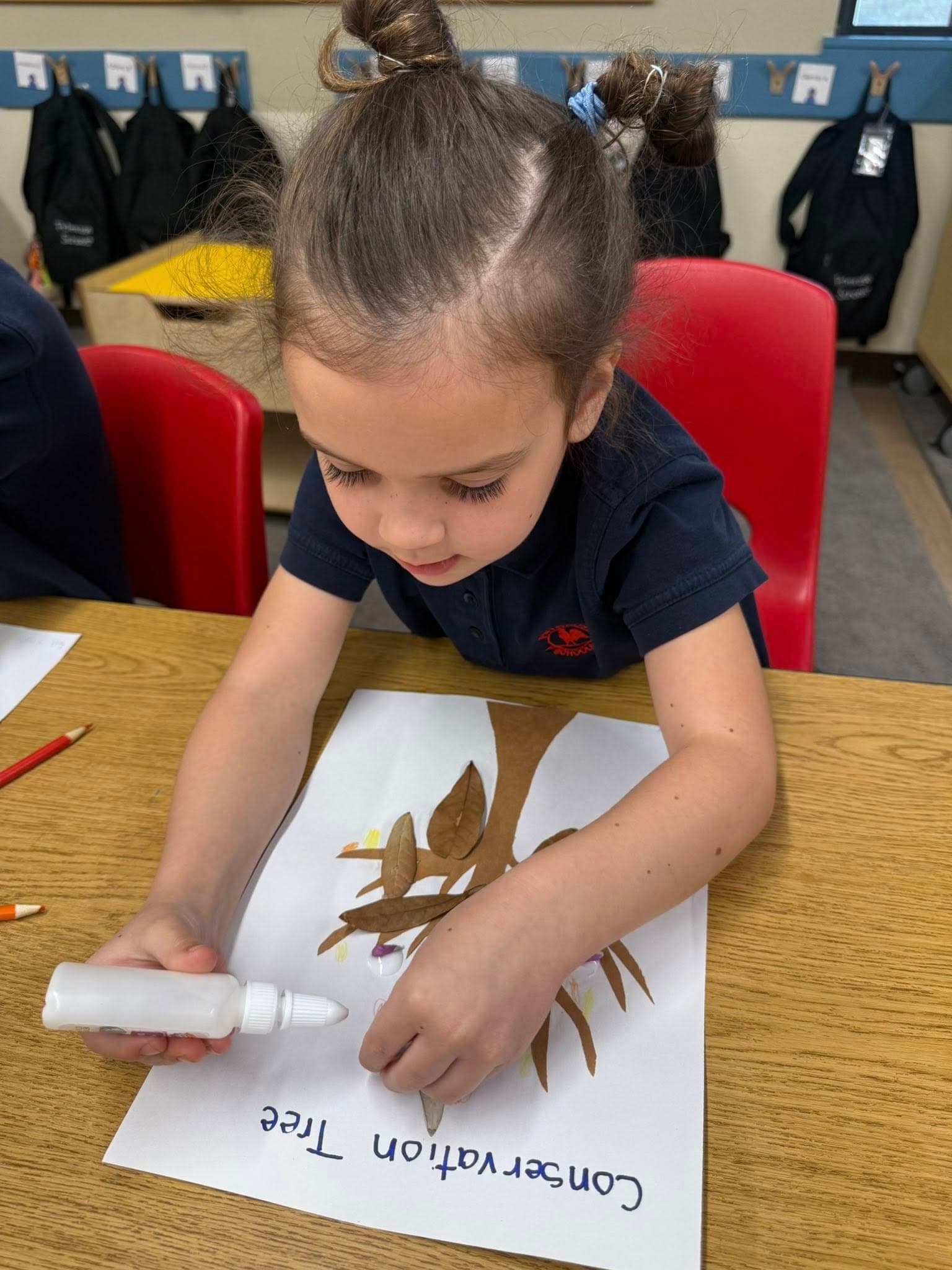 Student creating a conservation tree collage using real leaves, glue, and paper while learning about nature and the environment.