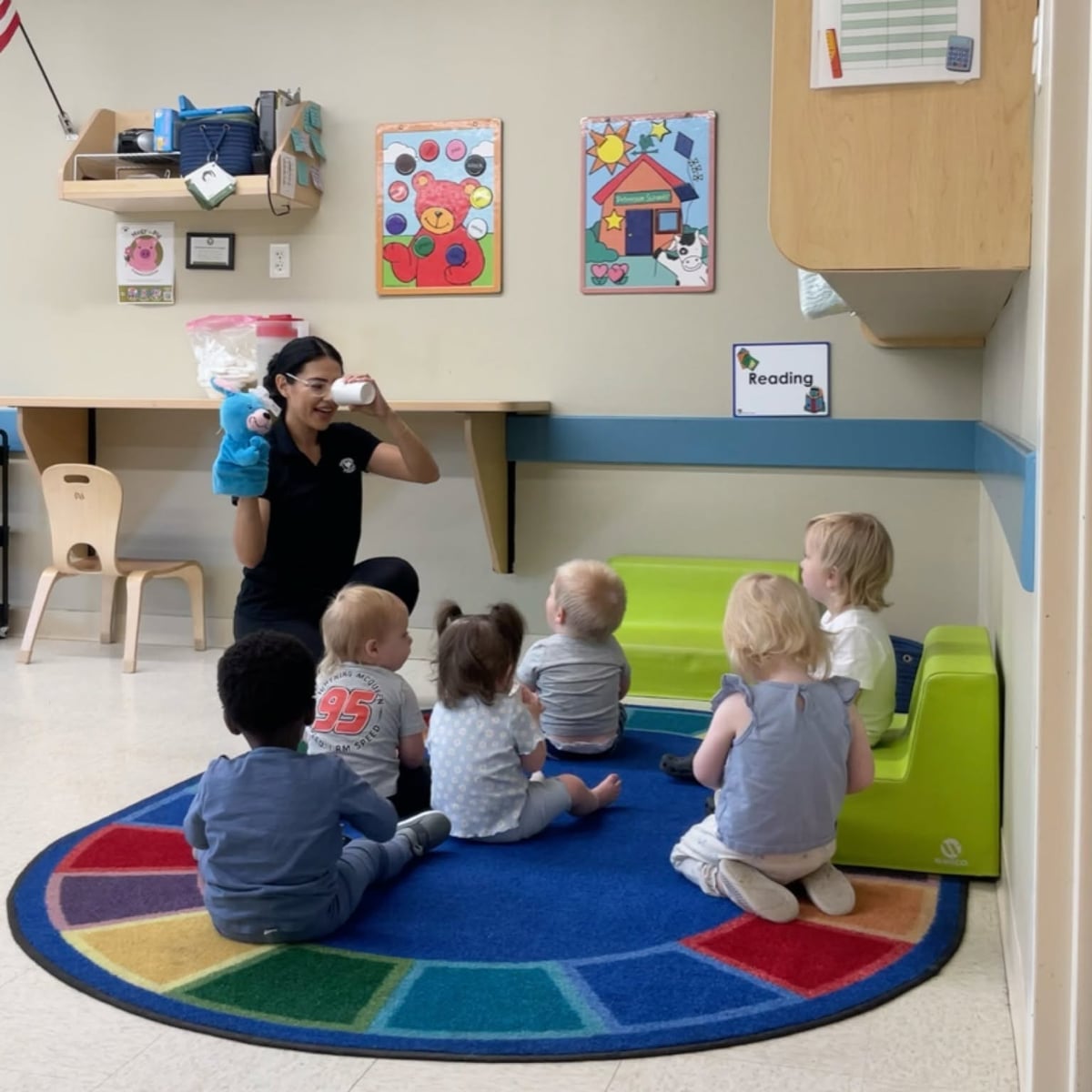 Teacher leading toddlers through an engaging circle time using songs, puppets, and imaginative play to encourage language development, social skills, and active participation at Primrose School.