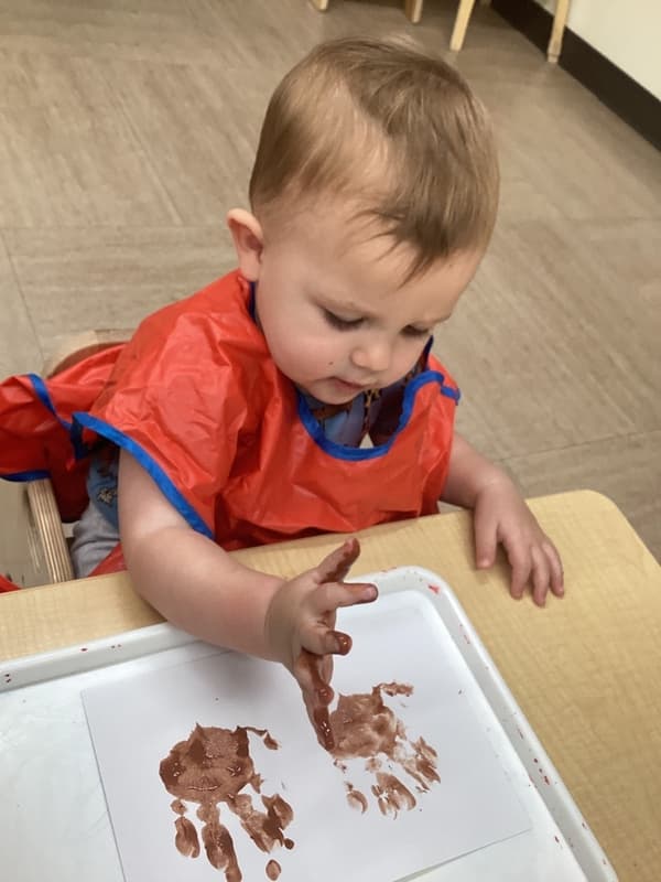 Infant creating a handprint painting project while exploring sensory art and developing fine motor coordination.