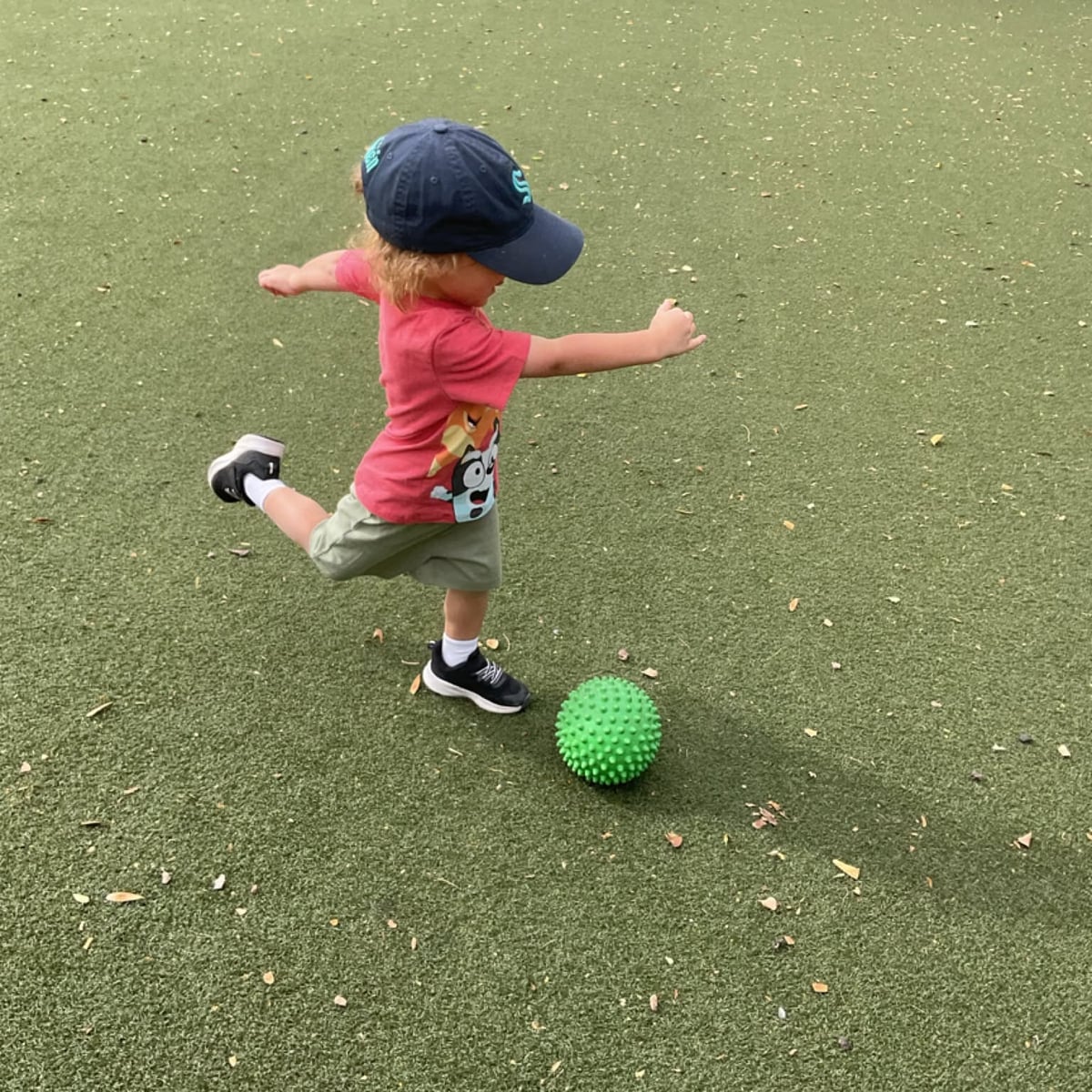 Toddler kicking a ball outdoors while strengthening balance, coordination, gross motor development, and confidence through active play at Primrose School.