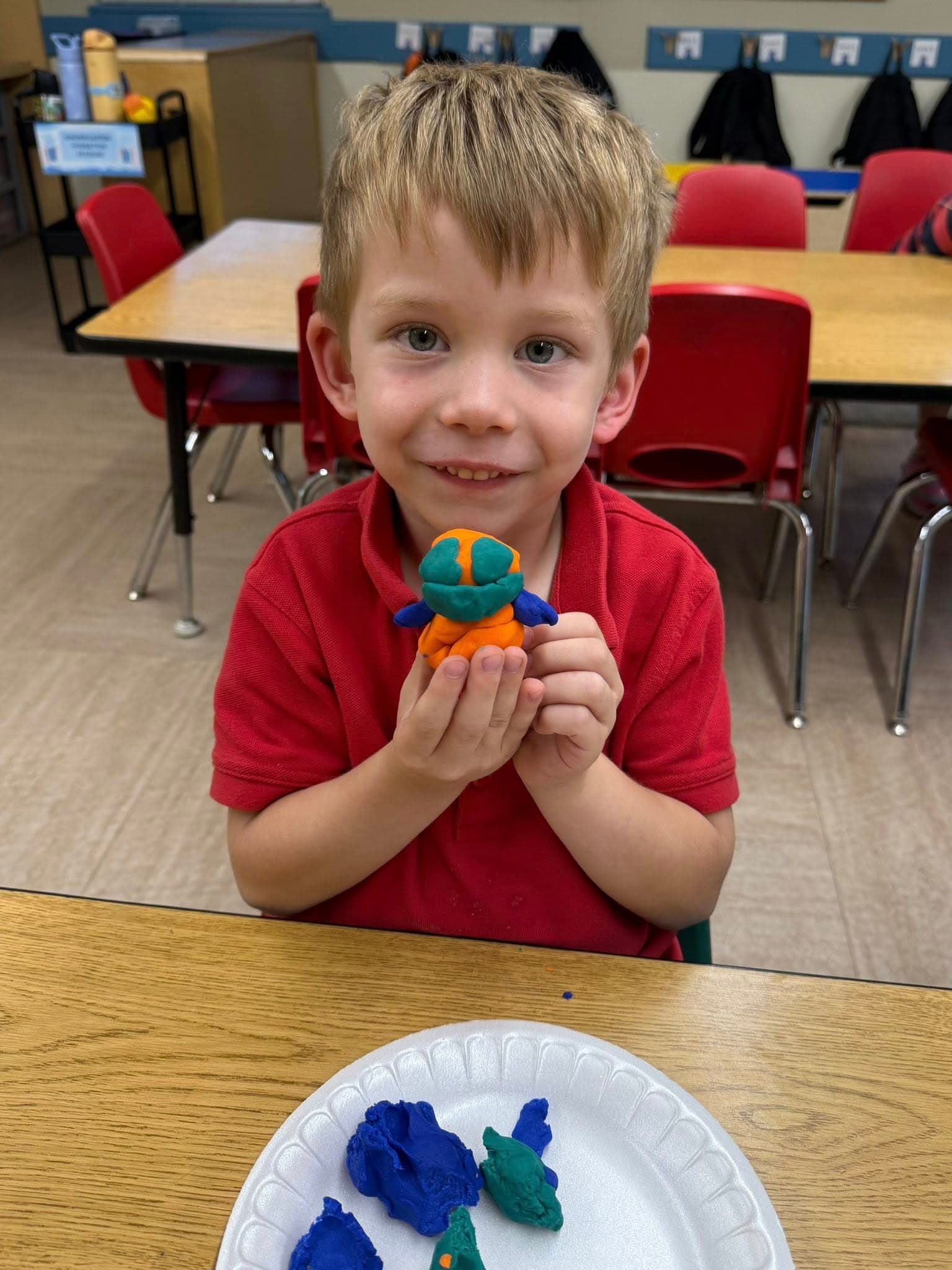 Preschool student proudly showing a colorful playdough creation made during a hands-on fine motor and creative arts activity.