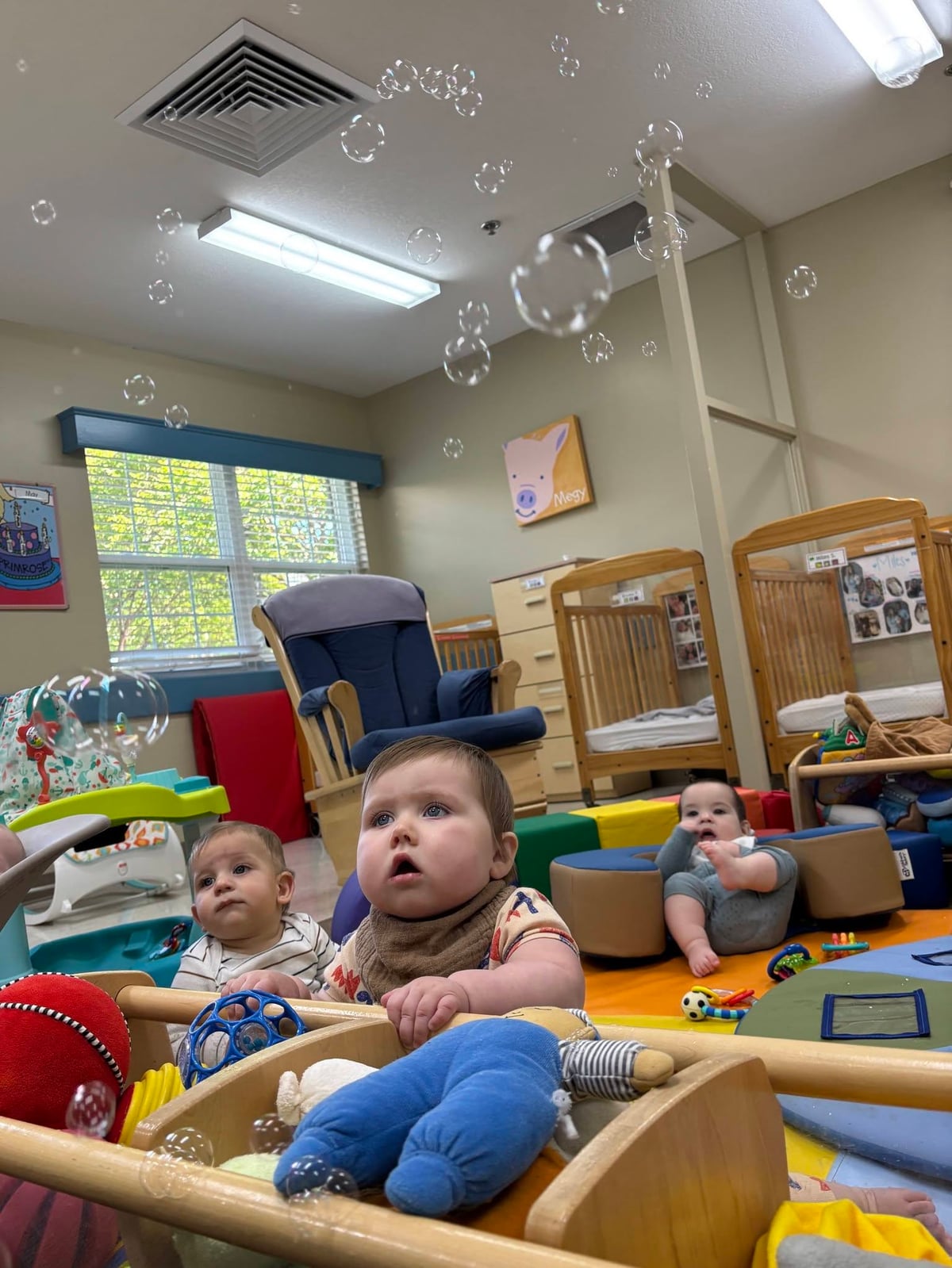 Infants watching and reaching for floating bubbles during a classroom sensory activity that encourages visual tracking, curiosity, and early motor skill development at Primrose School.