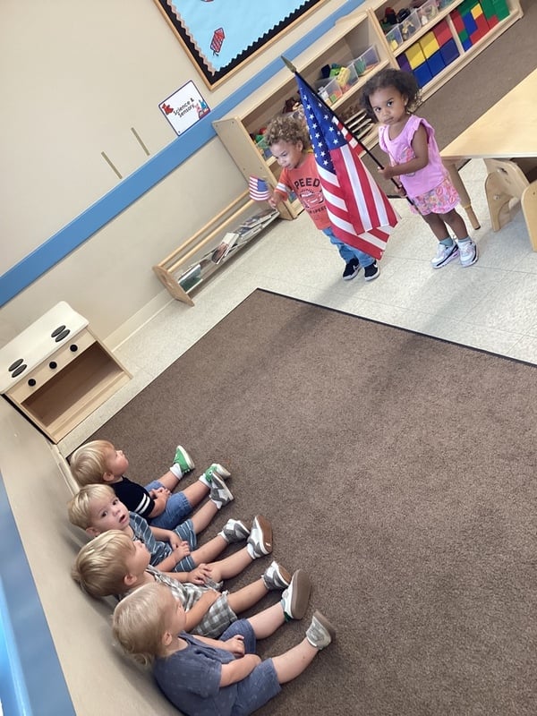 Toddler children doing the pledge of allegiance and holding the american flag in their classroom at fort worth childcare center.