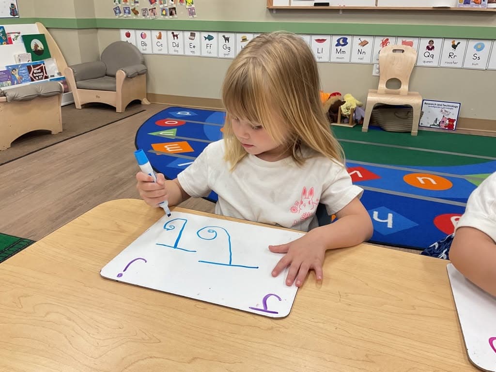 Young child practicing number writing on a whiteboard during a math lesson focused on number recognition, formation, and early numeracy skills.