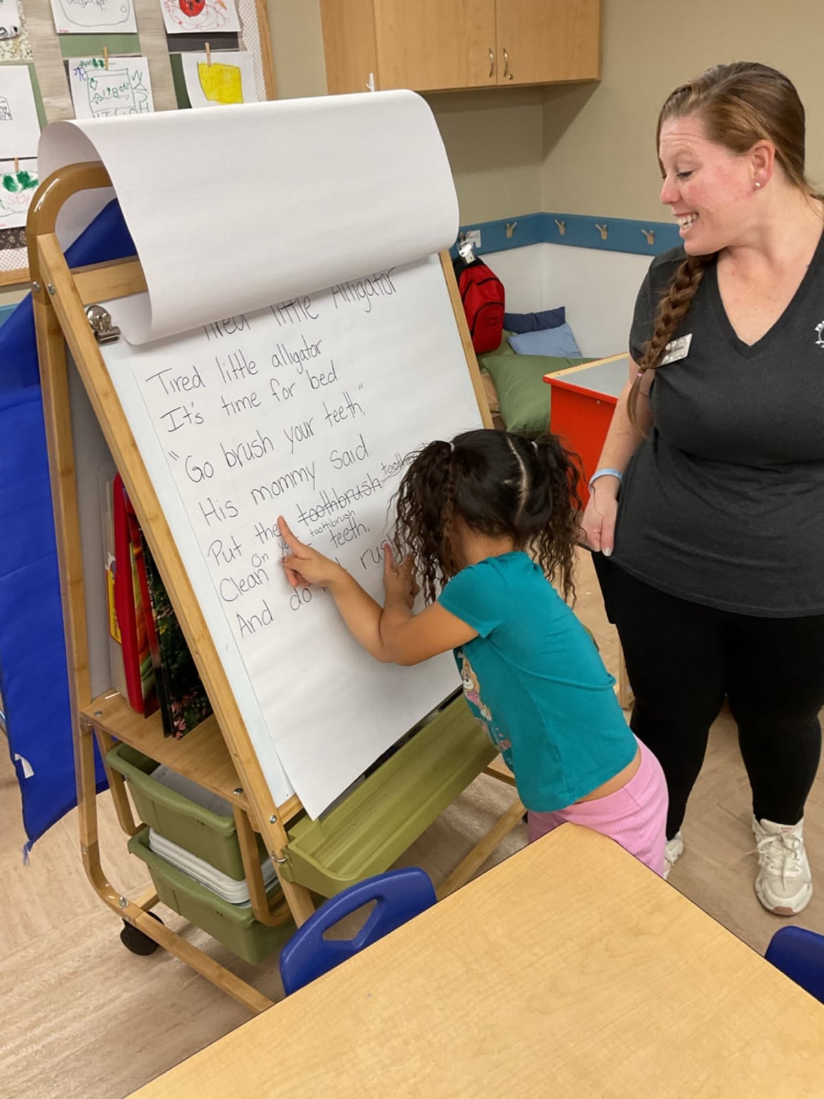 Primrose teacher helps a preschool student practice letter recognition and early literacy during a small-group classroom activity.