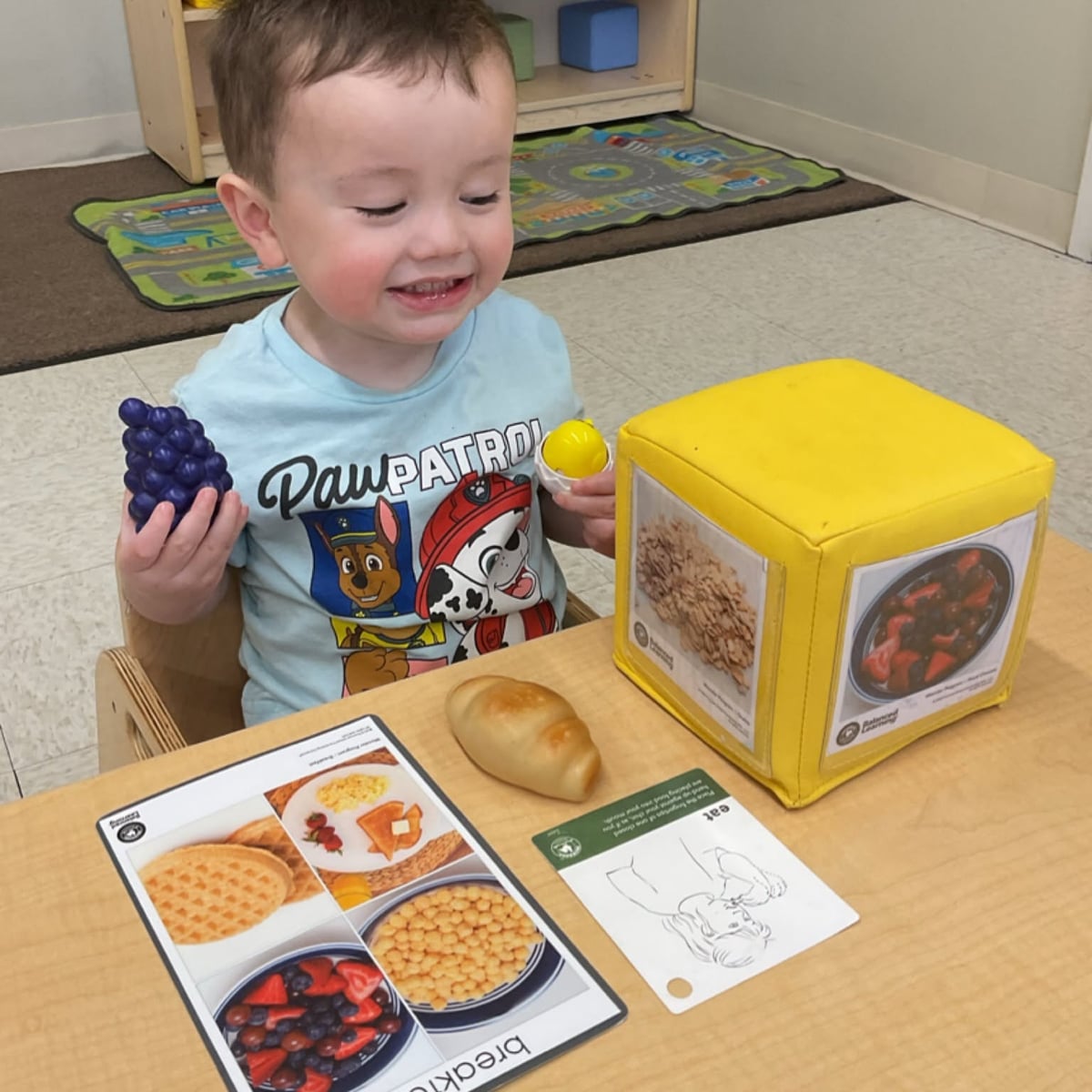Toddler using realistic food toys and matching cards to learn about healthy food choices while developing language, sorting, and early nutrition concepts at Primrose School.