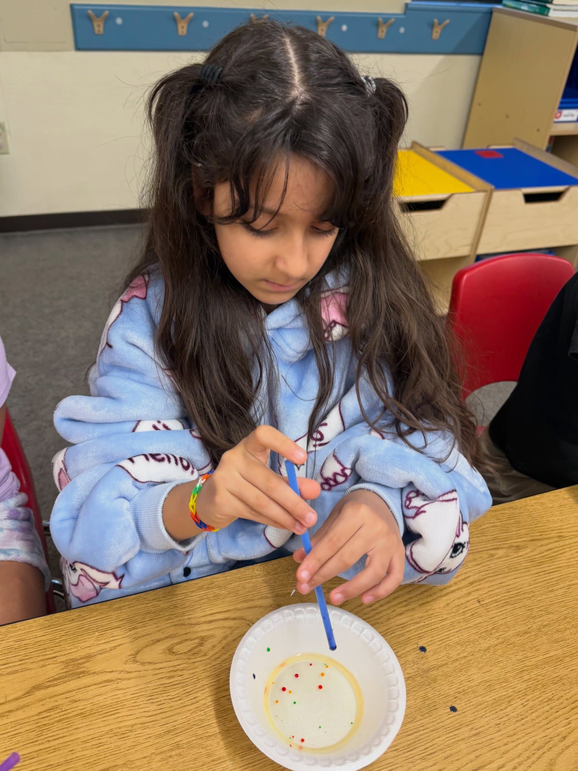 Student using a straw to observe and experiment with floating objects during a classroom science exploration activity.
