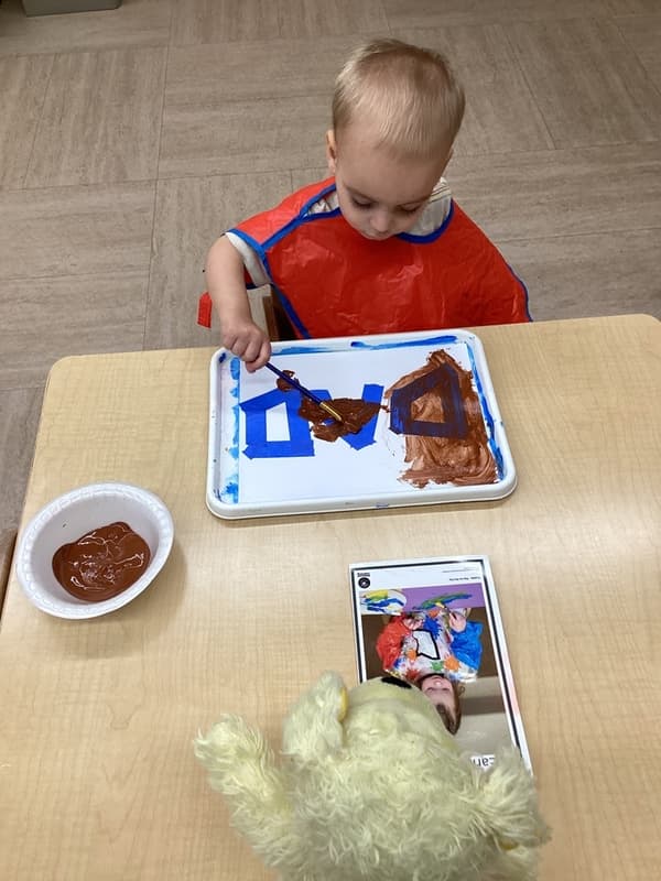 Toddler using a paintbrush to fill in shape outlines during a hands-on art activity that supports creativity and shape recognition.