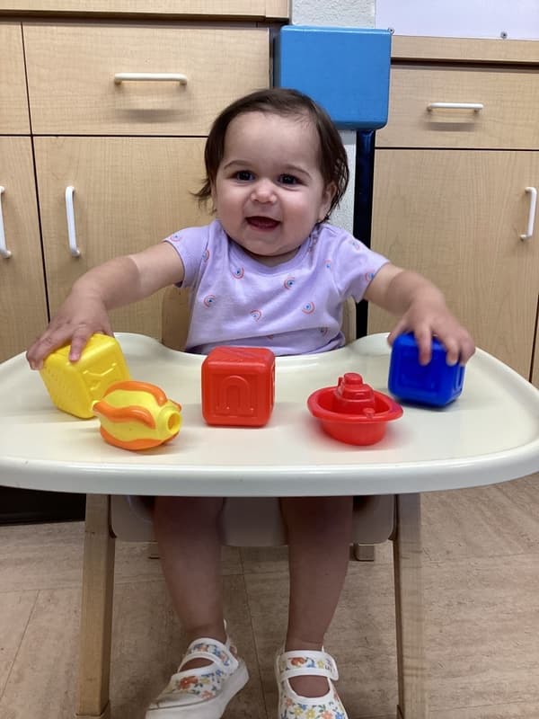 Infant playing with colorful stacking and shape toys while developing hand-eye coordination and fine motor skills through interactive play.