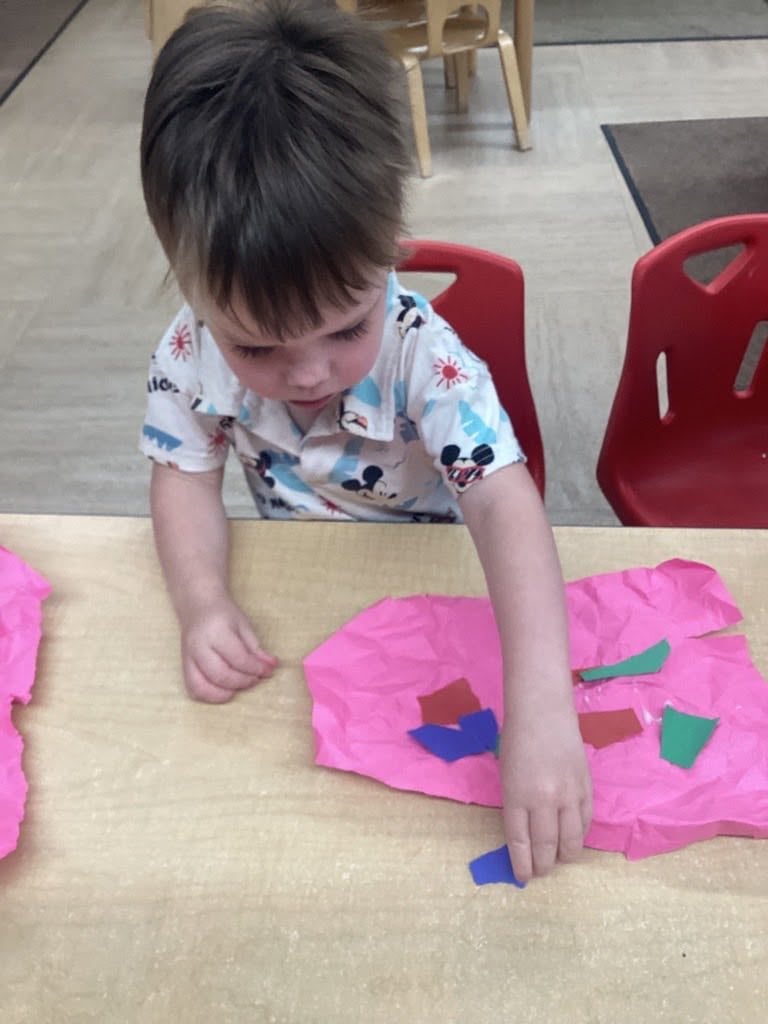 Toddler arranging colorful tissue paper pieces to create a collage during a hands-on art activity that builds creativity and fine motor skills at Primrose School.