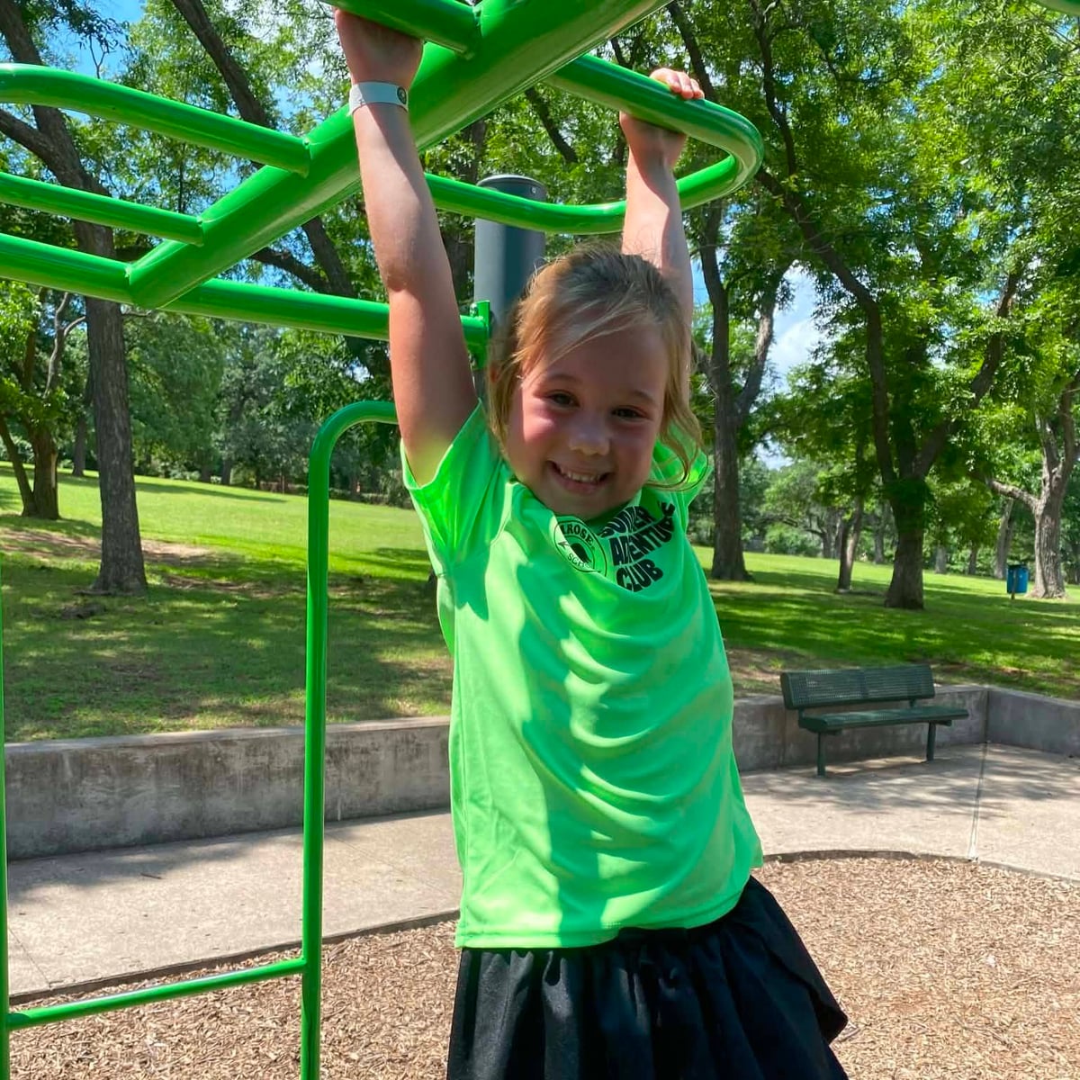 A Summer Adventure Club student winkging on the monkey bars in the park on a field trip with Primrose School at Heritage.