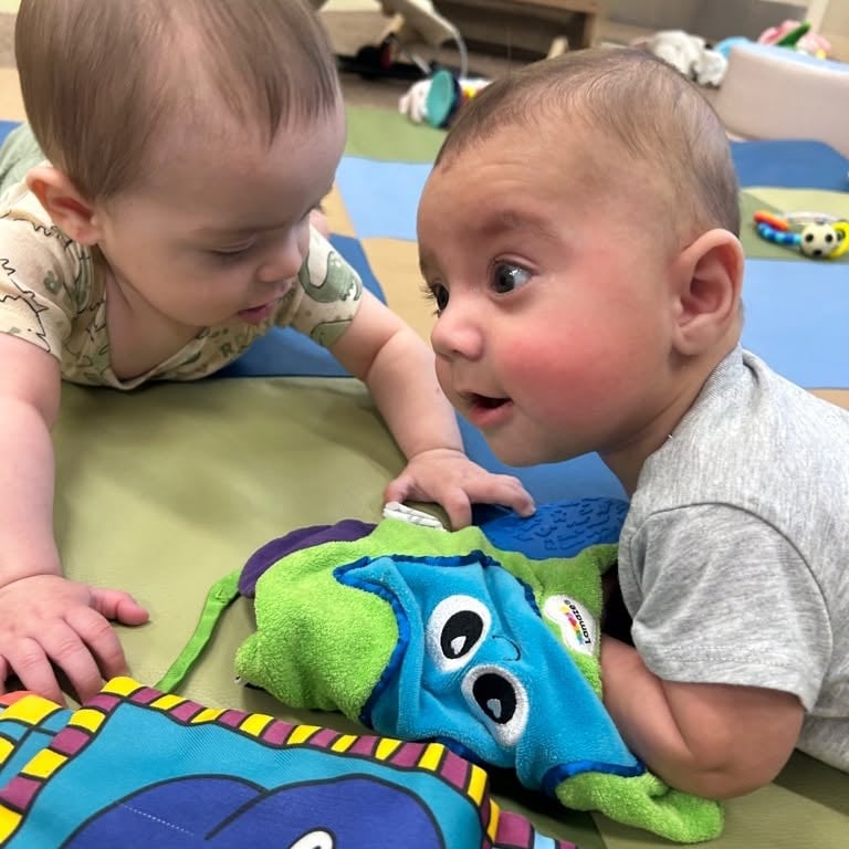 Two infants engaging in tummy time together while exploring soft sensory toys to strengthen muscles, encourage movement, and support early social interaction at Primrose School.