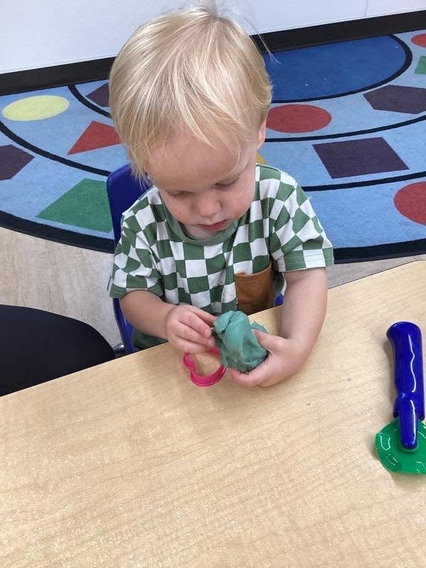 Toddler exploring playdough with classroom tools during a sensory activity that strengthens creativity, hand muscles, and fine motor development at Primrose School.