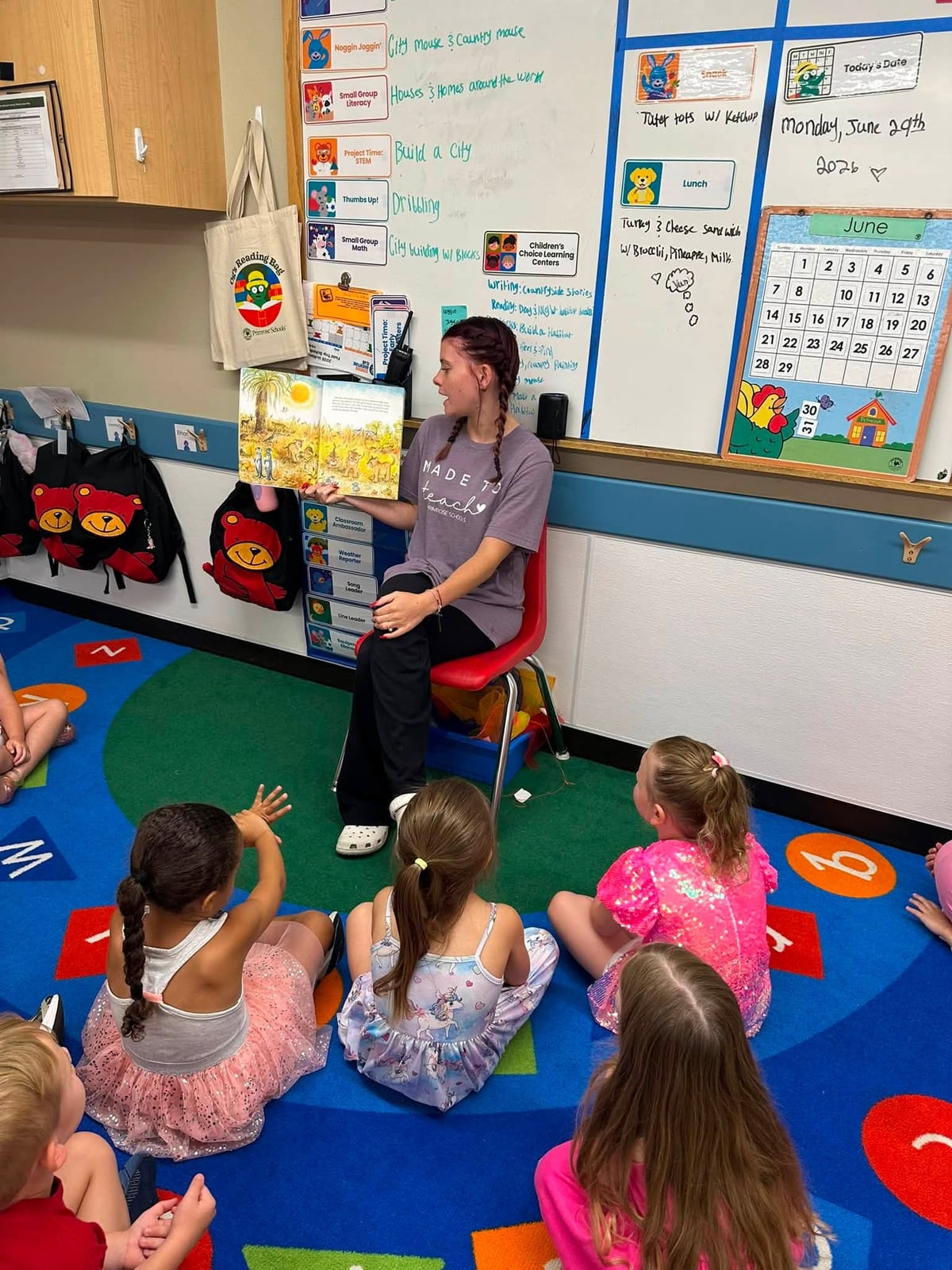 A Primrose School teacher reads a picture book to a group of preschool students gathered on a colorful classroom rug during story time, encouraging literacy, imagination, and classroom engagement.