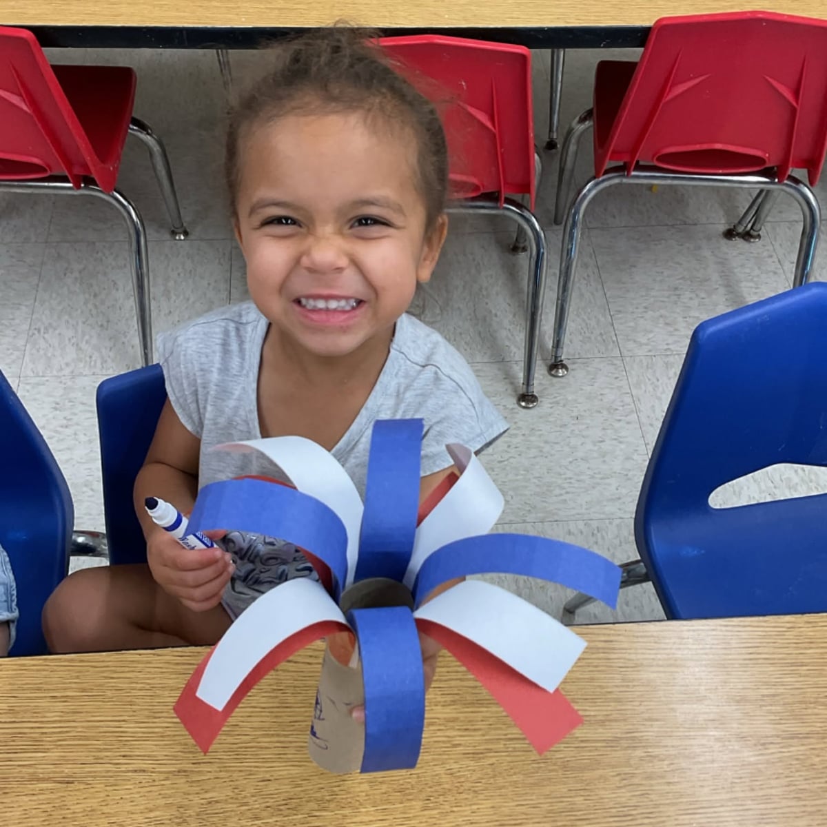 Preschool student creating a colorful red, white, and blue craft to strengthen creativity, fine motor skills, and artistic expression during a classroom activity at Primrose School.