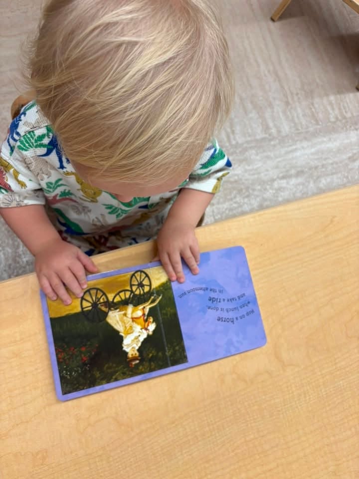 Toddler looking through a board book during independent reading time to build early literacy skills and a love of books at Primrose School.