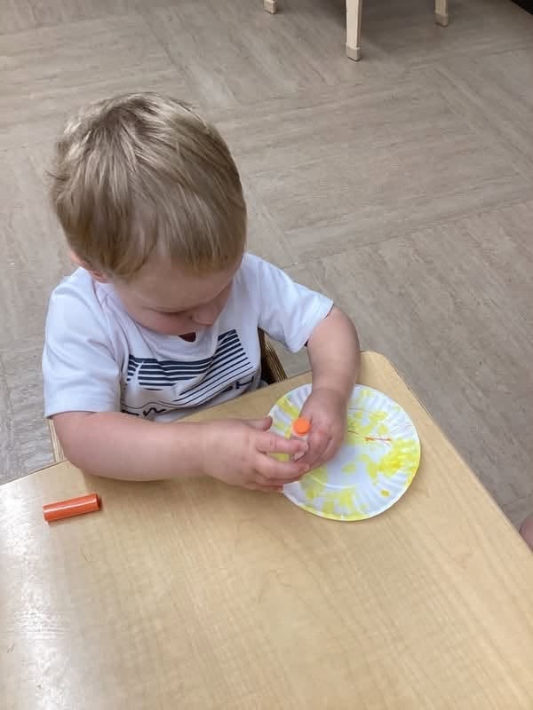 Toddler decorating a paper plate with paint during a process art activity that strengthens creativity and fine motor skills at Primrose School.