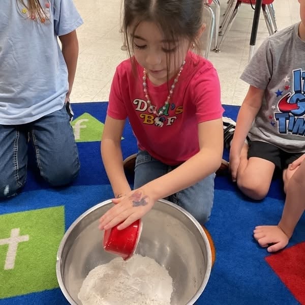 Preschool student participating in a hands-on cooking activity, measuring ingredients to build early math skills, following directions, teamwork, and confidence at Primrose School.