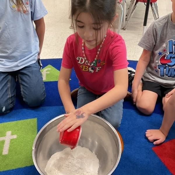 Preschool student participating in a hands-on cooking activity, measuring ingredients to build early math skills, following directions, teamwork, and confidence at Primrose School.