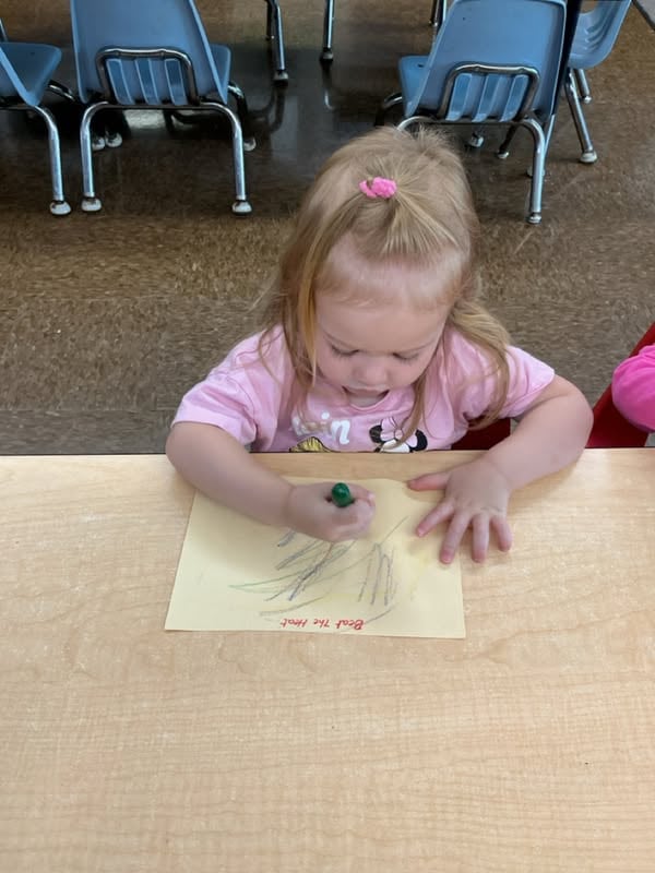 Toddler using a crayon to create marks on paper during a pre-writing activity that strengthens fine motor development, hand-eye coordination, pencil grip, and early literacy readiness at Primrose School.