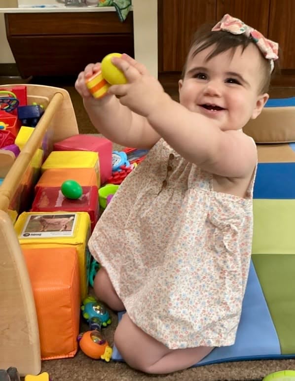 Smiling infant playing with colorful stacking toys to develop fine motor skills, hand-eye coordination, and early problem-solving at Primrose School.