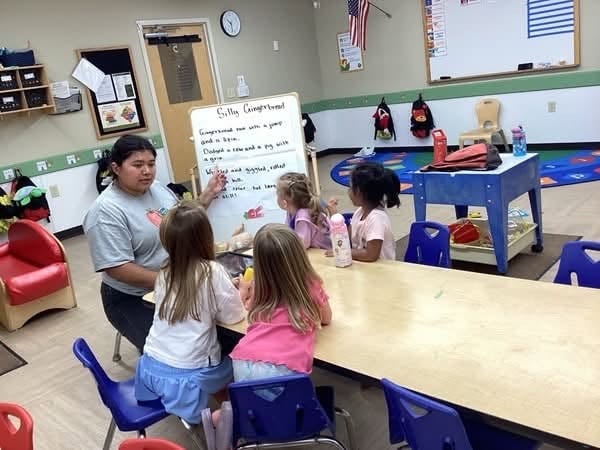 Primrose teacher leading a small group learning activity with preschoolers during circle time to encourage communication, listening, and early literacy development.