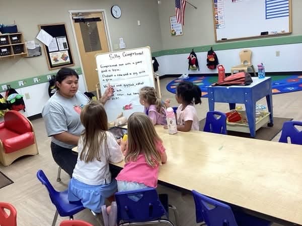 Primrose teacher leading a small group learning activity with preschoolers during circle time to encourage communication, listening, and early literacy development.
