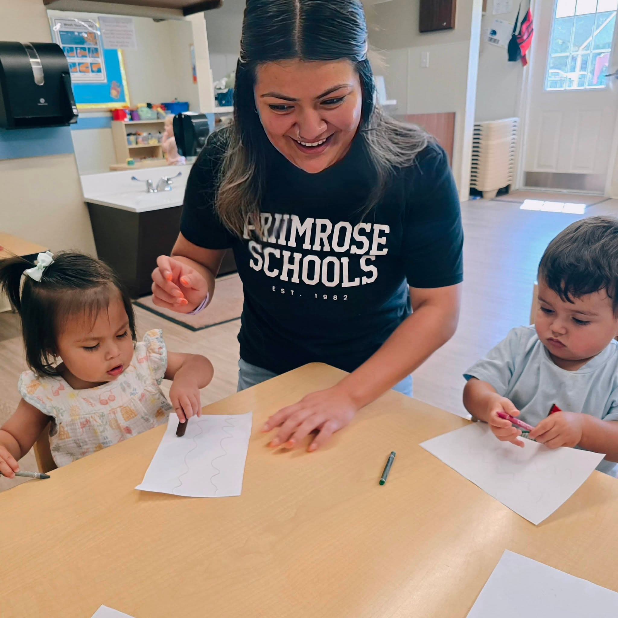 A toddler teacher smiling and engaging with students in her daycare class during a small group at Primrose School at Heritage on Heritage Trace Parkway.