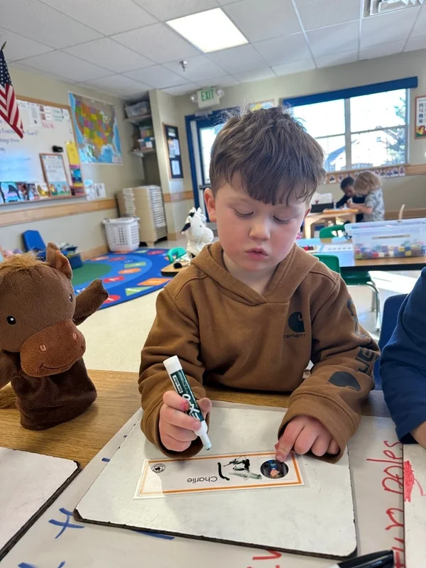 a boy learning to write his name in the preschool classroom.