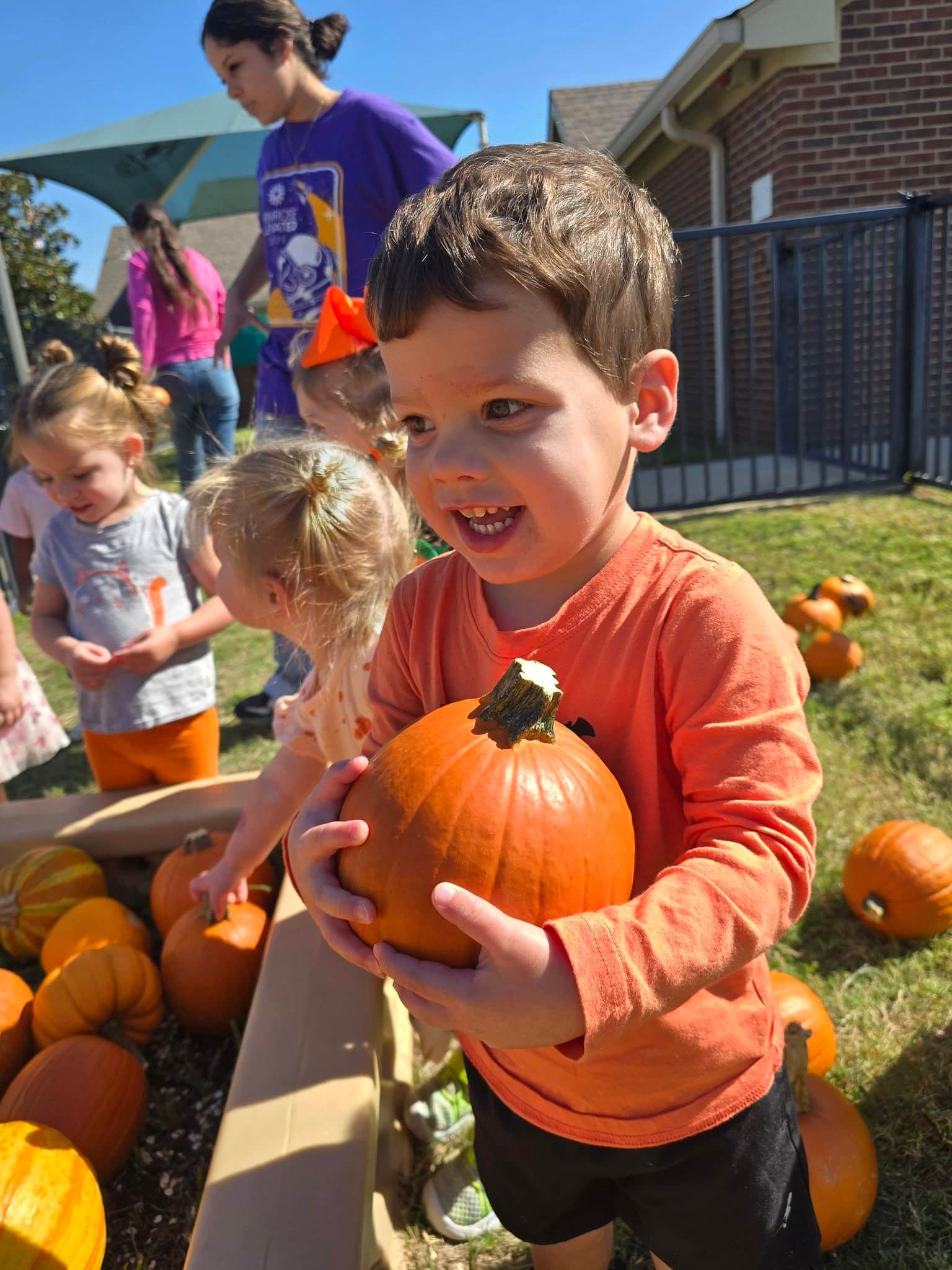 Young student holding a pumpkin in the Primrose Patch at Primrose School at Heritage in Fort Worth, TX, enjoying a fun autumn activity at our preschool and daycare