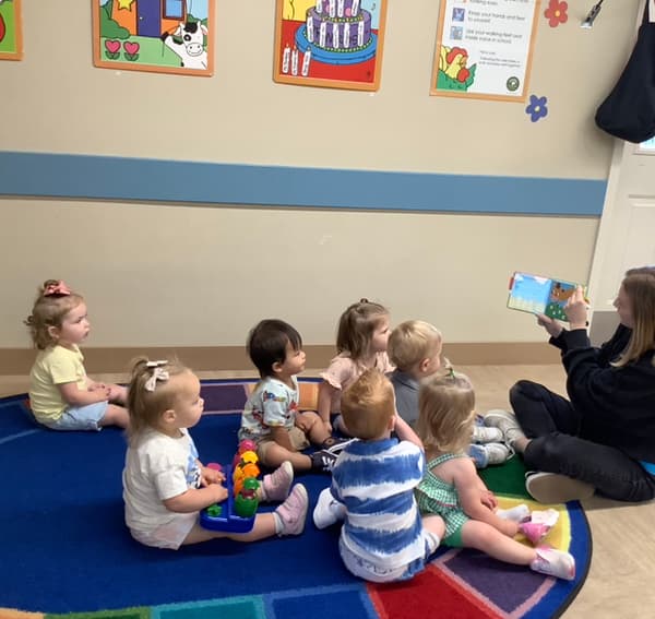 Infants and toddlers group story time with their teacher. Early literacy, social development, and classroom engagement in a nurturing preschool environment.