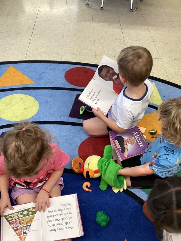 Preschool children exploring books together during group reading time while learning about healthy foods and early literacy concepts.
