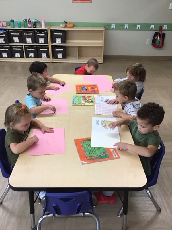 Children sitting at a table creating pictures of their families.