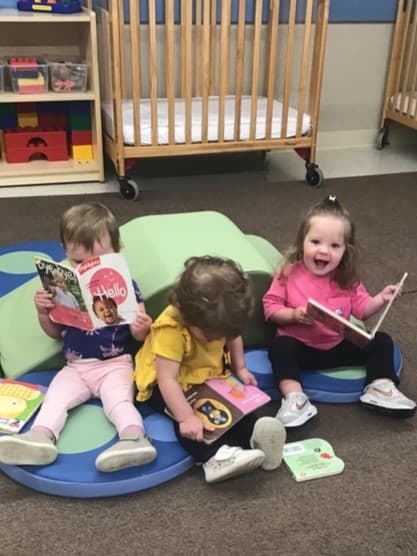 Three toddler children practicing early literacy skills with books at Fort Wolrth Daycare