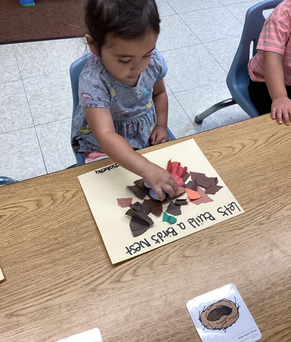 Child creating a bird's nest craft with torn paper pieces during a hands-on nature-themed learning activity in the classroom.