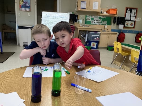 Two Pre-K students observing colored liquids in test tubes during a science activity at Primrose School of Thornton