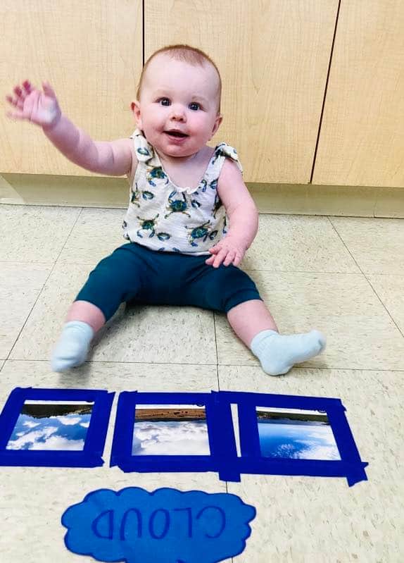 infant baby sitting in front of images of clouds learning about weather and science at Primrose in North Fort Worth.