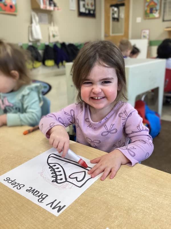 little girl smiling and coloring a shoe with a marker