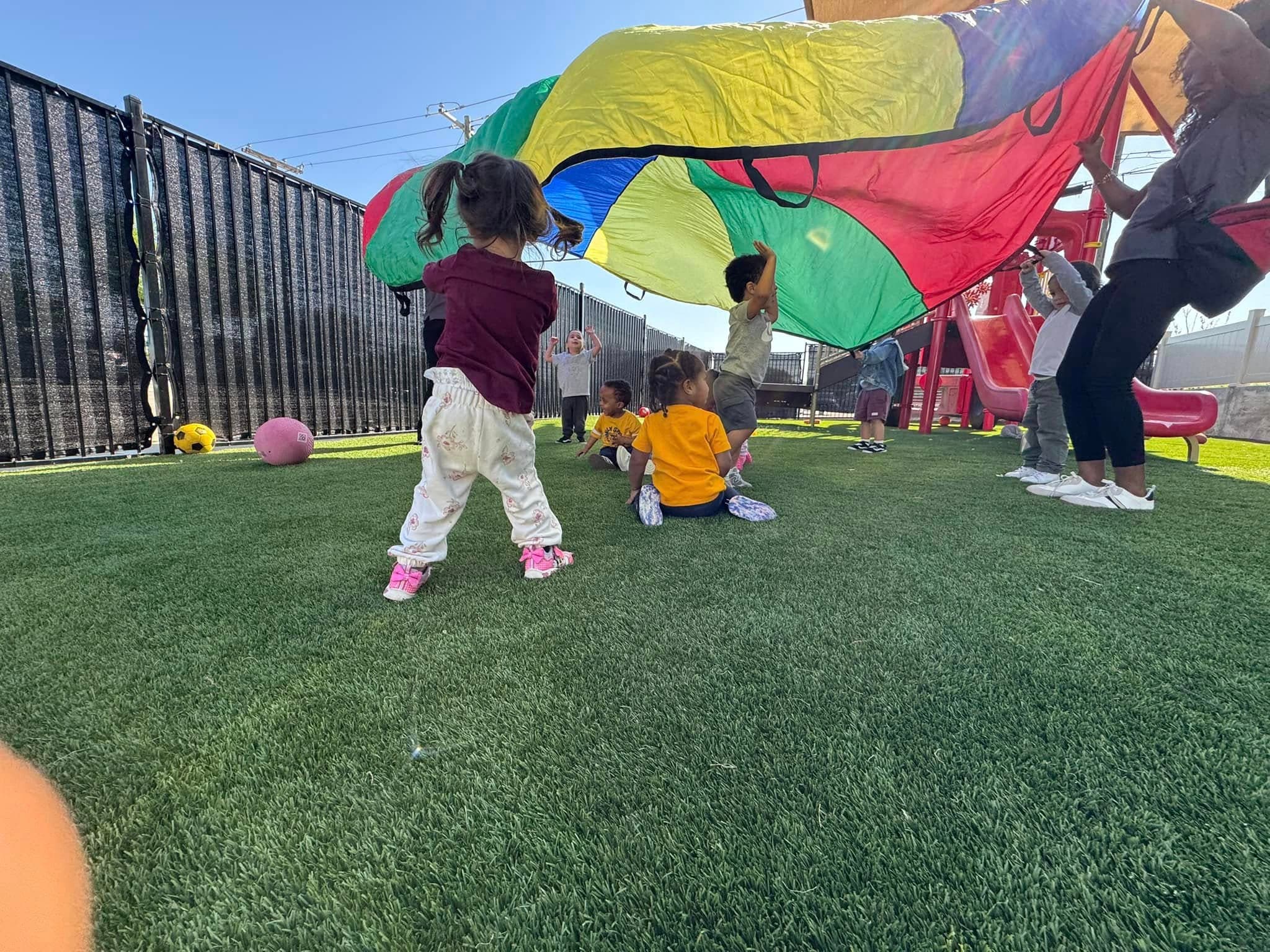 children and teacher on a playground, playing with a colorful parachute
