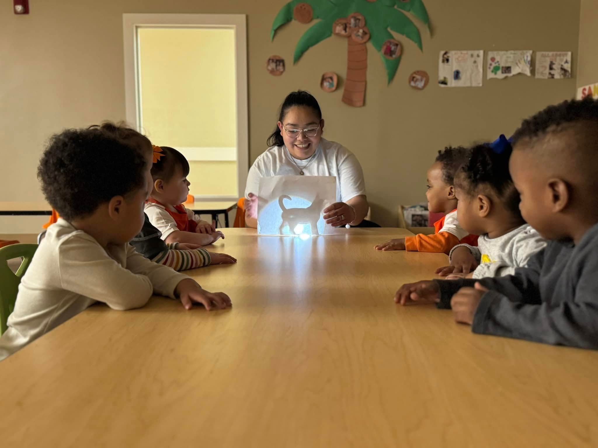 children sitting at a table with teacher, creating shadow puppets