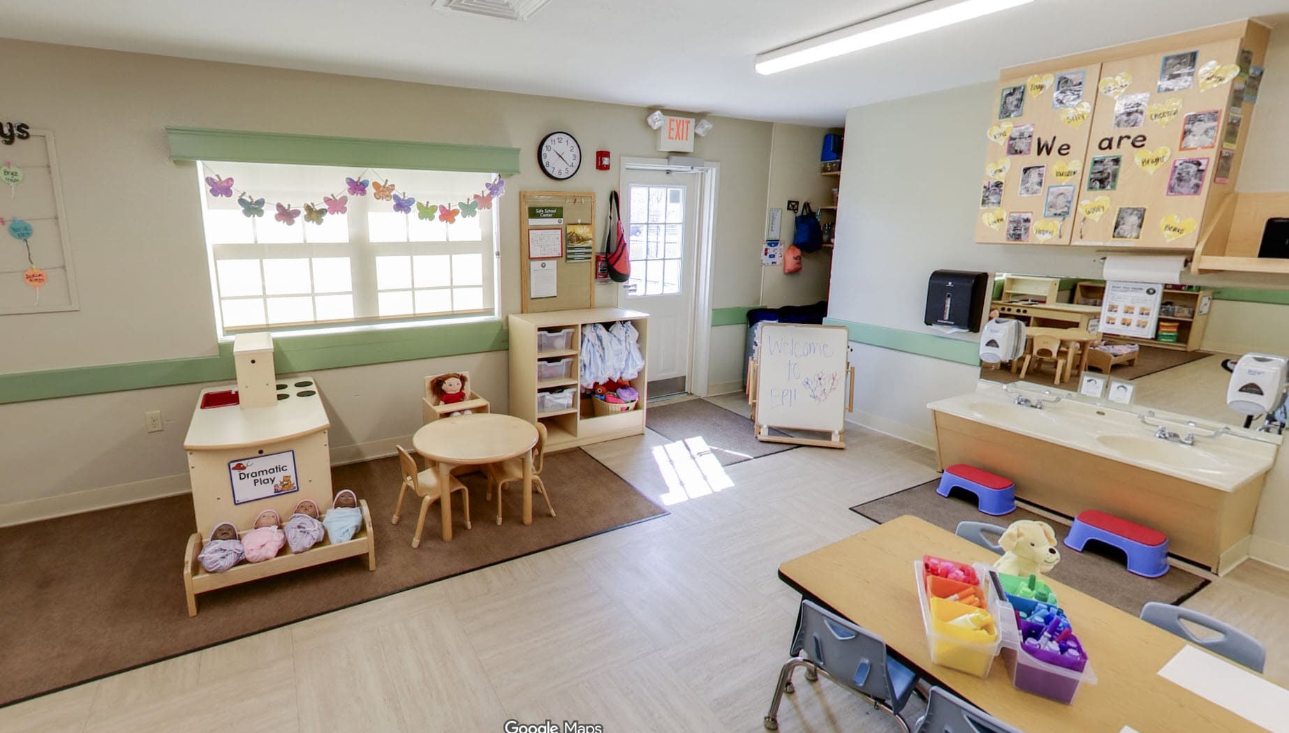 Primrose School of Eagan early preschool classroom featuring a dramatic play area, butterfly garland, round table with chairs, learning centers, dedicated handwashing sinks, and a "We Are" children's display board.