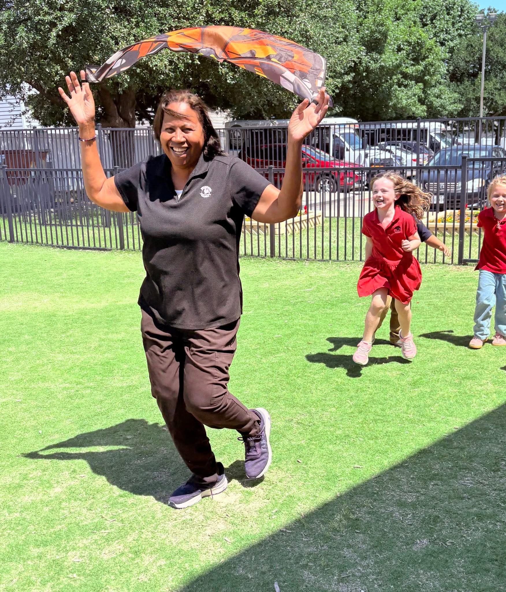 teacher running around with butterfly wings while kids chase her