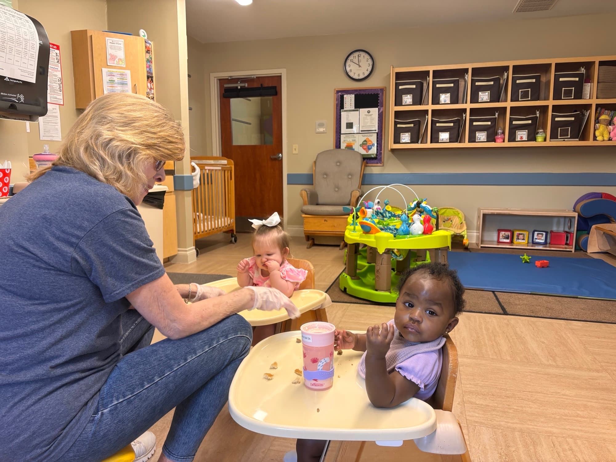 Ms. Diane sits with two infants in highchairs as they enjoy a meal from our healthy menu at Primrose School at Summerwood