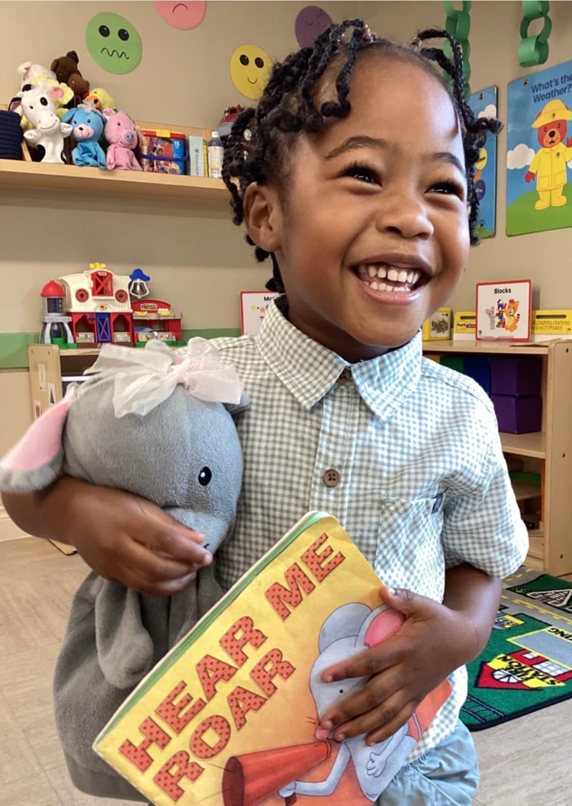 a smiling little boy, holding on to Mia the Mouse and her book, "Hear Me Roar"