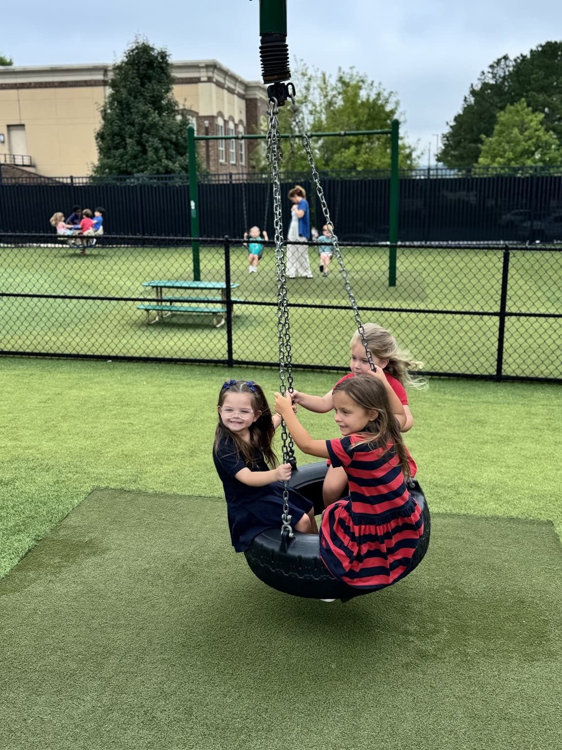 Primrose School of Braselton students smiling and playing together on a tire swing during outdoor playground time.