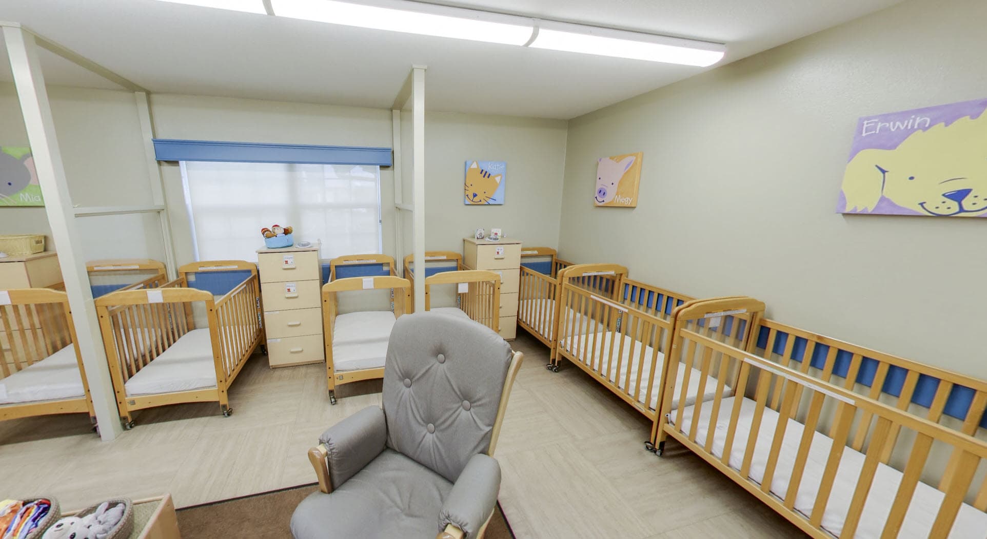 Primrose School of Eagan infant classroom featuring individual cribs, a comfortable rocking chair, natural light, and Primrose Friends character artwork in a calm, clean environment.