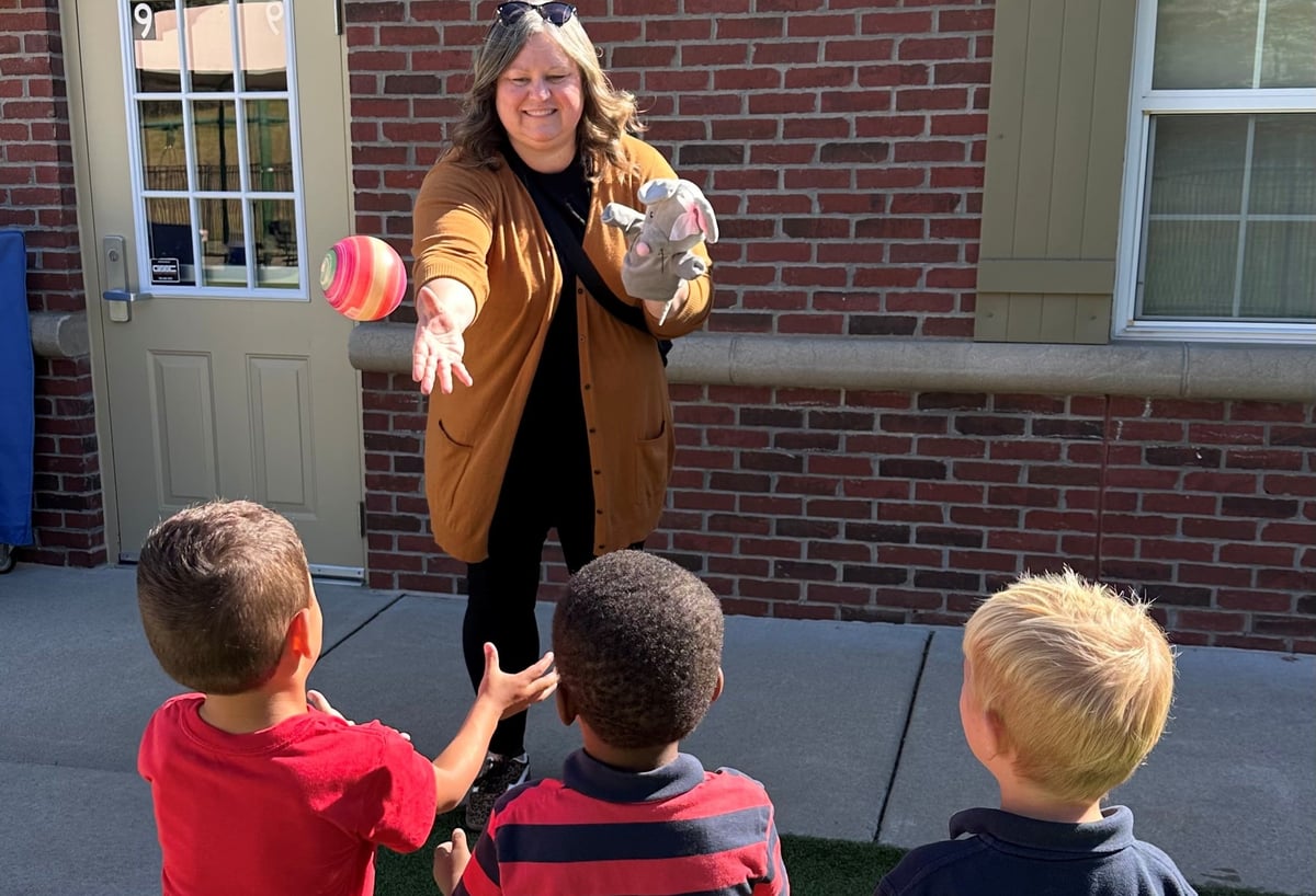 Preschool teacher playing catch with three children during puppet character development play at Primrose School of Eagan